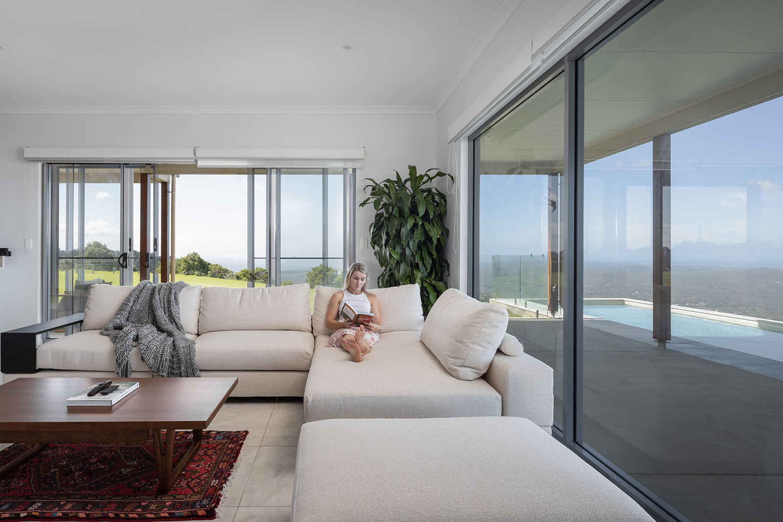 Living room with large windows and a view of an outdoor swimming pool and lush landscape on the Sunshine Coast.