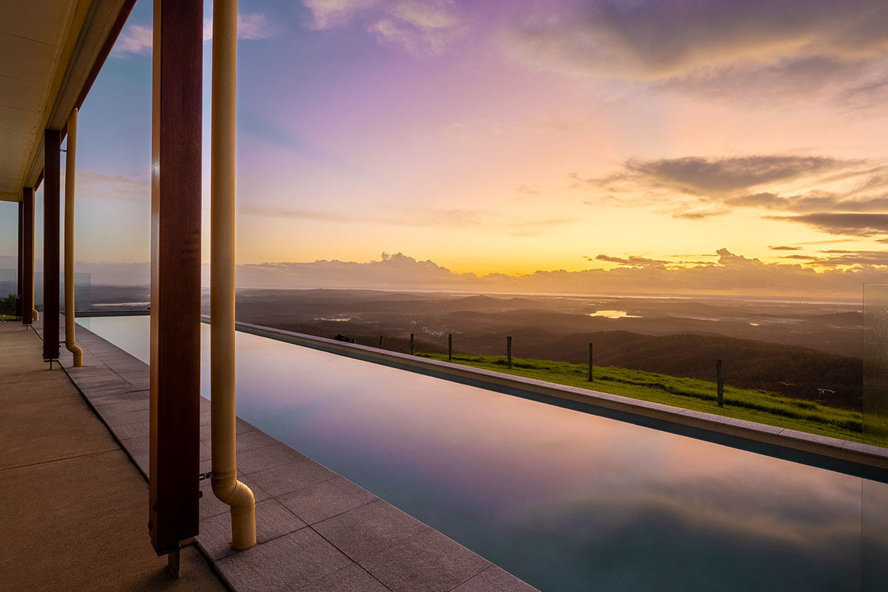 Petrichor Estate has a long lap pool that overlooks the ocean and rainforest, offering stunning 360-degree views of a vast landscape and colourful sunset sky.